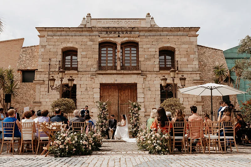Ceremonia civil frente a la fachada de piedra de la bodega centenaria, novia y novio con invitados sentados
