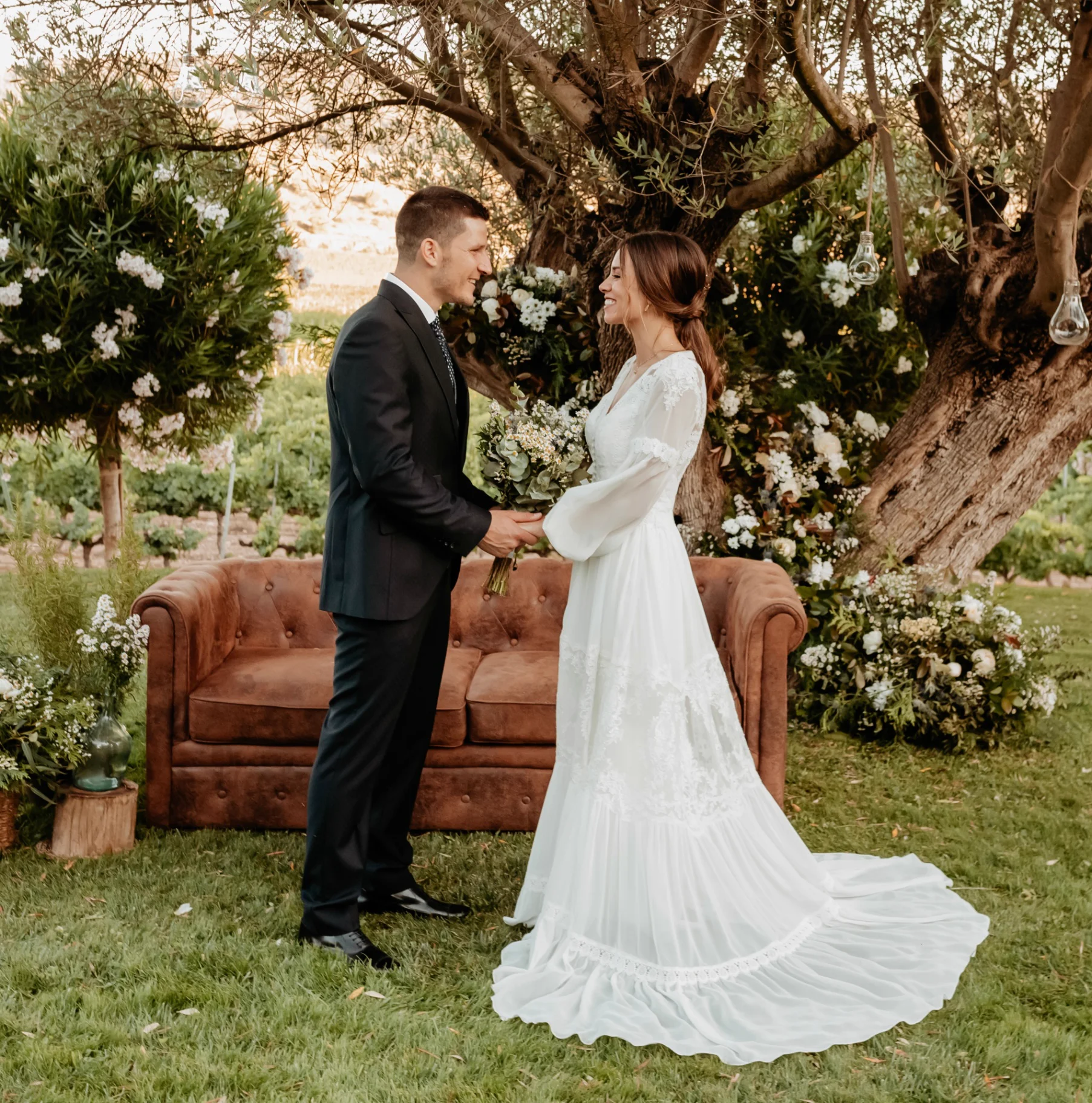 Pareja bajo olivo centenario en el jardín de la finca, sofá de cuero y decoración floral
