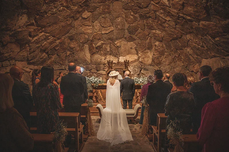 Novia y novio en el altar de la capilla de piedra con invitados